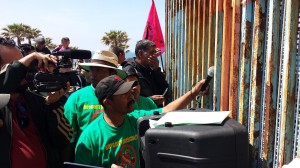 Ayudado con un micrófono para escuchar el mensaje de los jornaleros del lado de San Ysidro, un trabajador agrícola mexicano recoge la voz que viene del otro lado. Foto: Rubén Tapia.