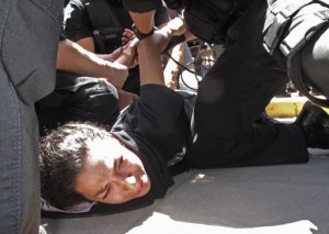 La manifestante que muerde polvo expresaba su repudio a Donald Trump, que realizaba un mitin en Fresno, California, cuando le cayeron –literalmente- encima los gendarmes. Foto: www.hickoryrecord.com