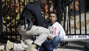 Un oficial de policía trata de liberar a un manifestante de inmigración que se encadenó a una puerta en. Foto: Washington Times.