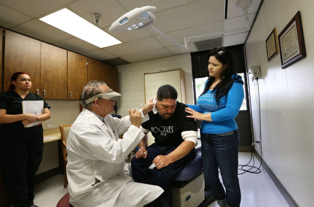 El Dr. David Elbaum ayuda a su paciente, Juan Solís, quien contrajo meningitis micótica en 2008; lo acompaña su esposa Julie durante la visita al dermatólogo en Bakersfield. Kenya Dávalos, auxiliar médico, ayuda al Dr. Elbaum.  Foto: Casey Christie / The Bakersfield Californian