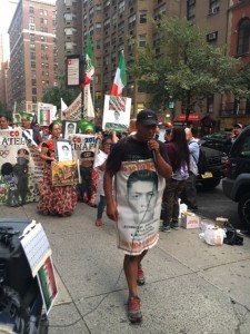 Al frente, Antonio Tizapa a la llegando al Consulado de México, con la foto de Jorge Antonio, su hijo desaparecido, ungida a su cuerpo. Micrófono en mano, hace un recuento ágil de los 5 años que han pasado sin conocer todavía el paradero de los normalistas. A sus espaldas viene la concejal Betina Cruz, encabezando la marcha.  