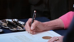 Se aprecia la mano de la líder de la mayoría demócrata en la Cámara de Representantes, Nancy Pelosi, firmando uno de los artículos del impeachment.