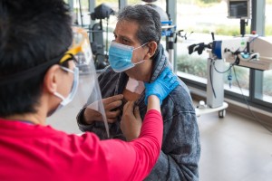 Speech pathologist Katherine Chan checks Vicente Perez Castro’s throat. He had a tracheotomy while in the hospital for covid. (Heidi de Marco / KHN).