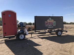 Una pancarta de Can II Ag Mgt. se encuentra junto a un baño portátil en un campo del condado de Fresno donde los trabajadores agrícolas dijeron que la empresa no les ofreció mascarillas N95 ni otras protecciones requeridas durante los días de mucho humo. Foto: Farida Jhabvala Romero/KQED.