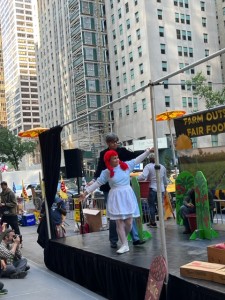  Gerardo Reyes representando a Nelson Peltz manipula a Nely Rodríguez (ambos organizadores de CIW), como si ésta fuera títere en un pasaje del teatro callejero frente a las oficinas principales de Trian Partners en Park Ave, de la Cd. de NY. Foto: MVG. 